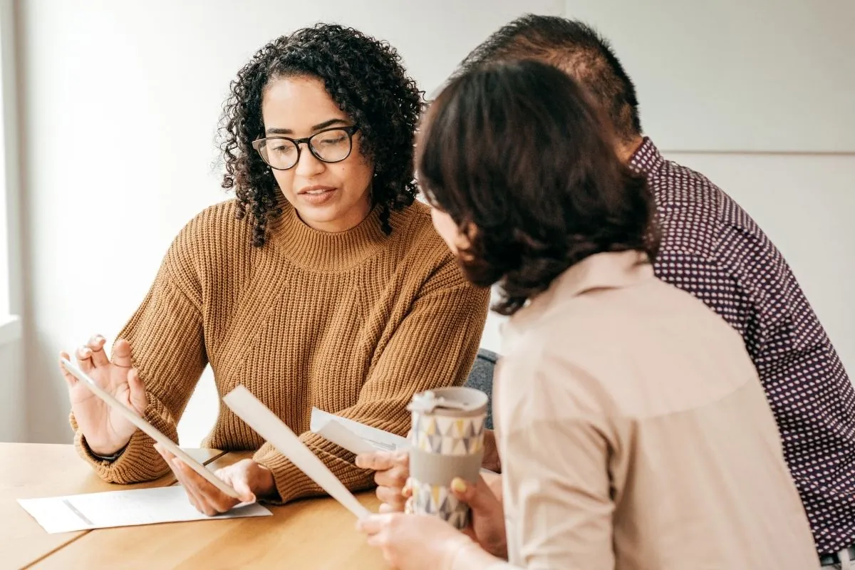 Three people in conversation over papers at a meeting table