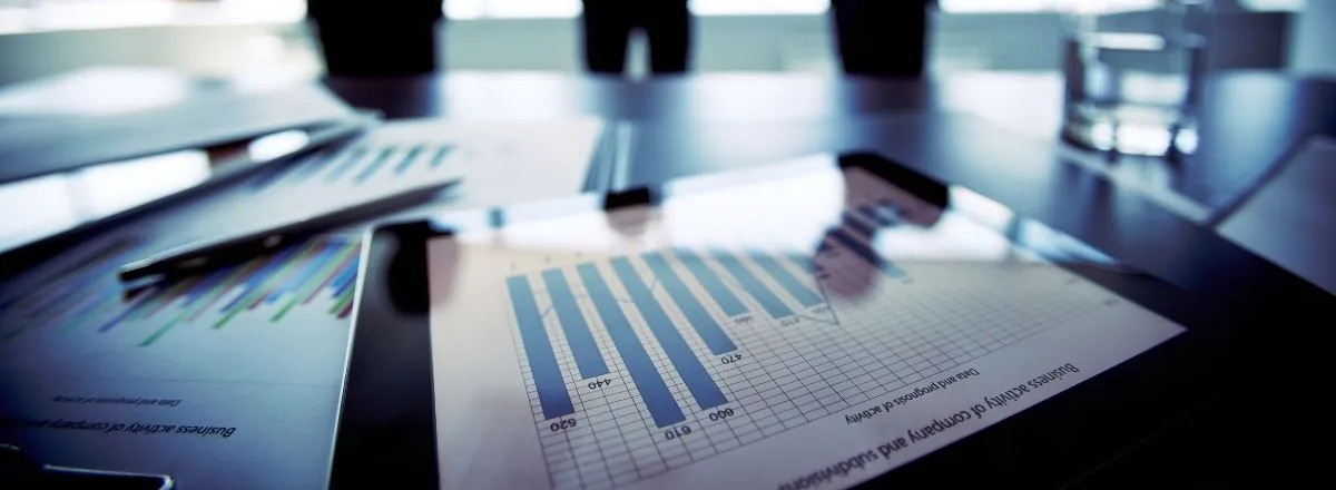 Market reports on a boardroom table with a meeting in progress behind